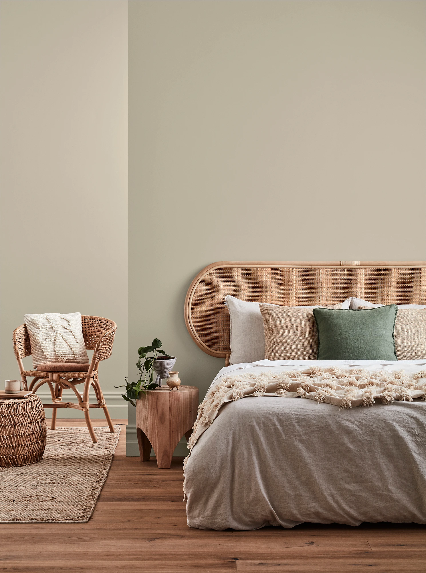 Neutral-coloured bedroom with rattan headboard and chair and neutral linens.