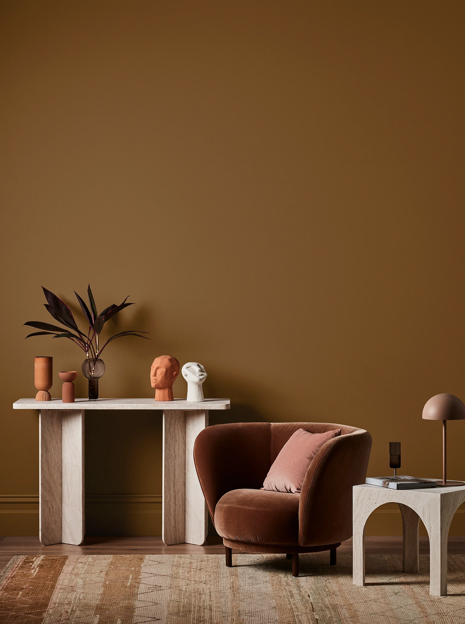 Brown living room with white console table with terracotta and white decor, velvet brown armchair and neutral side table with brown lamp. 