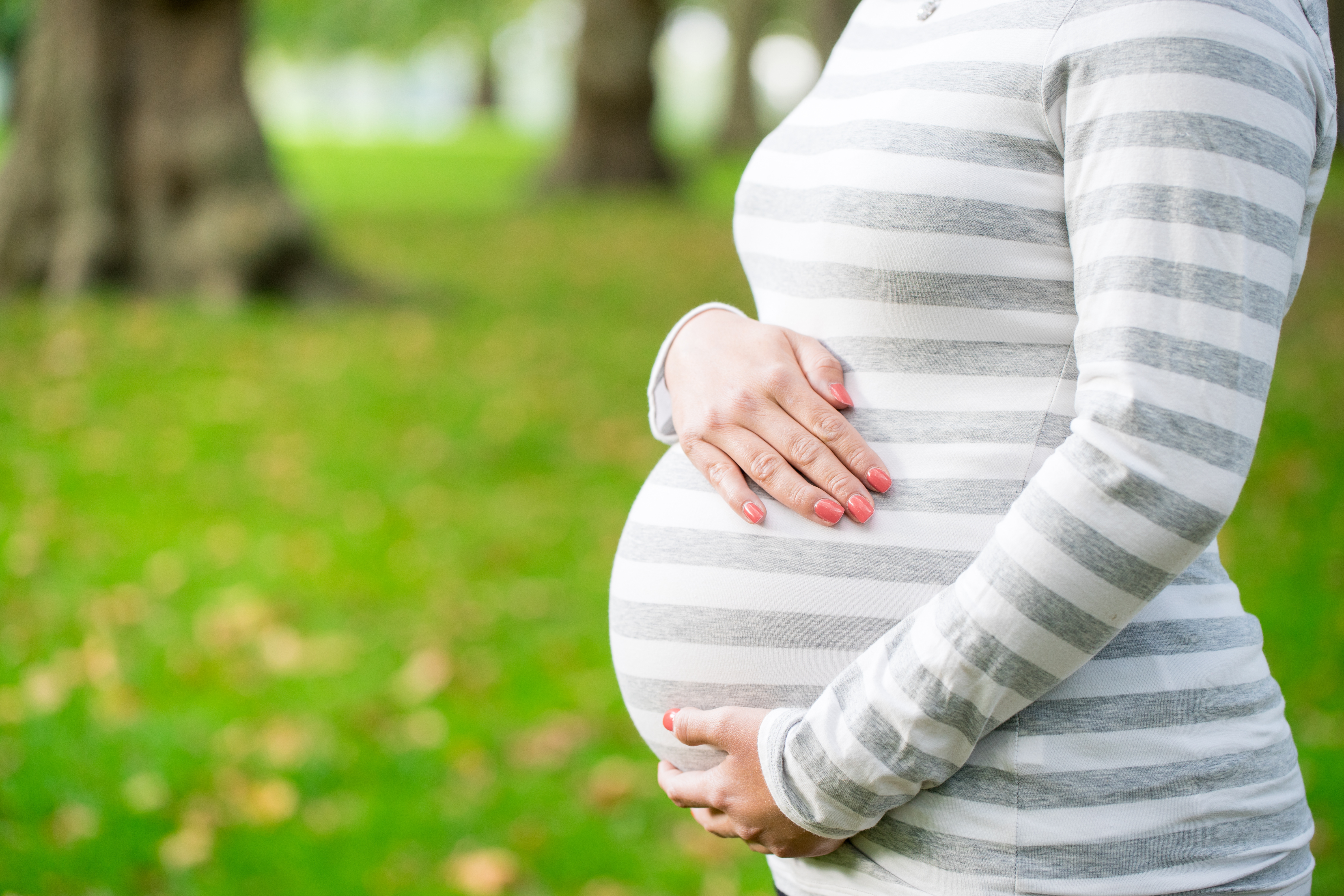 An expecting mother holds her pregnant belly in the park