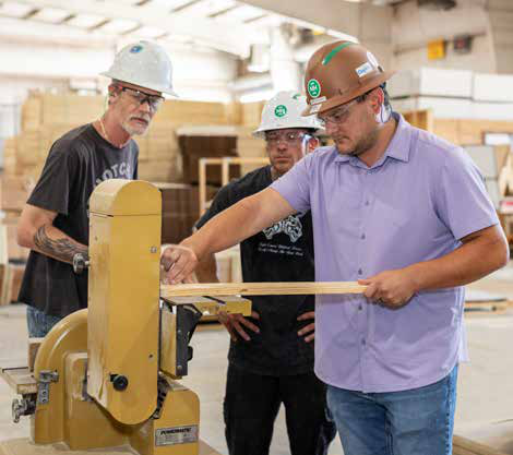 Joseph Coffee and Chase Kelley watch as Jayson Feres uses a band saw to cut lumber to size for a sturdy new twin bed.