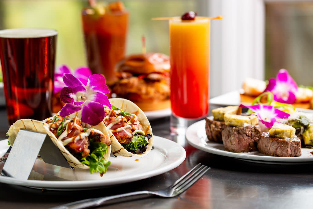 Flower-topped filet medallions and ahi tuna tacos are accompanied by a pint of craft beer and a vibrantly colored cocktail.