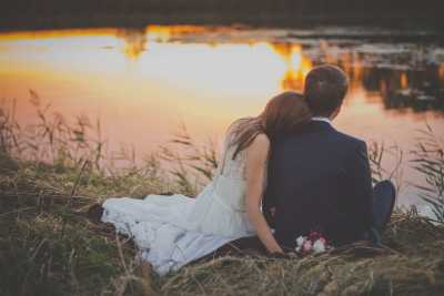 Bride and Groom sitting on the bank of a lake. 