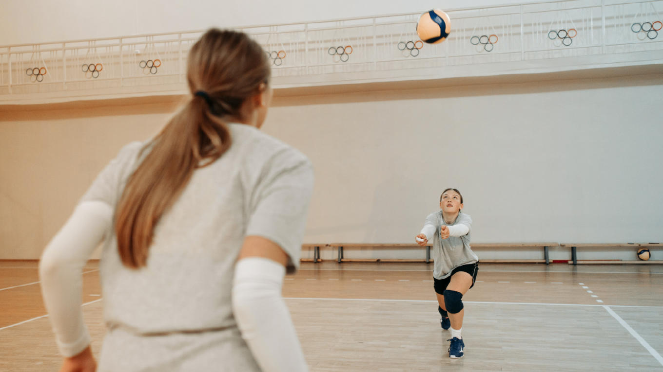 Two members of women's volleyball team run passing drills.