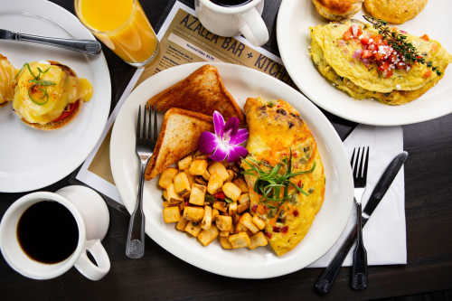 A spread of items from Azalea Kitchen's breakfast menu, including an omelette with home fries and toast, fresh-baked biscuits, eggs Benedict, and a mug of hot coffee.