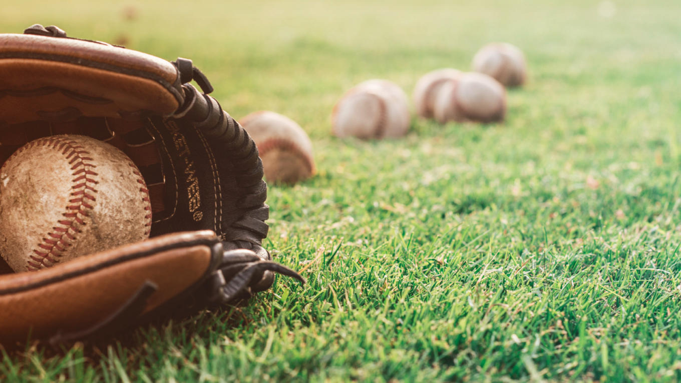 A baseball mitt and a few balls lay in the outfield grass after a game.
