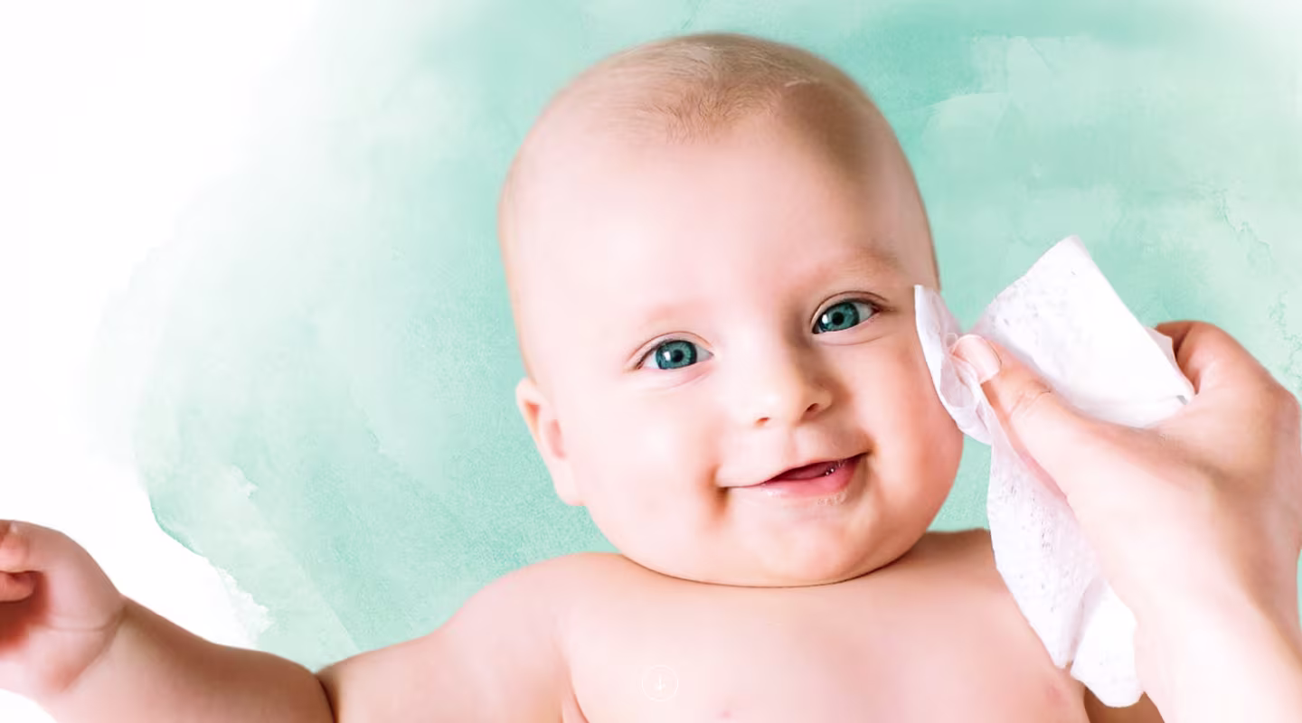 A close-up of a baby's face as a hand gently wipes their cheek with a Pampers® Complete Clean wipe.