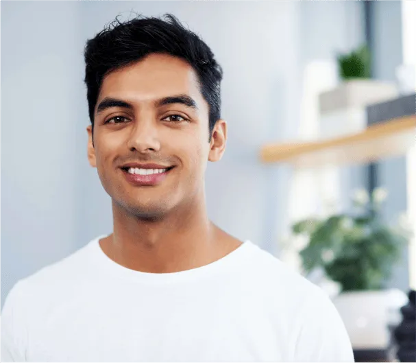 A picture of a young man in a white shirt in a well lit room with plants in the background