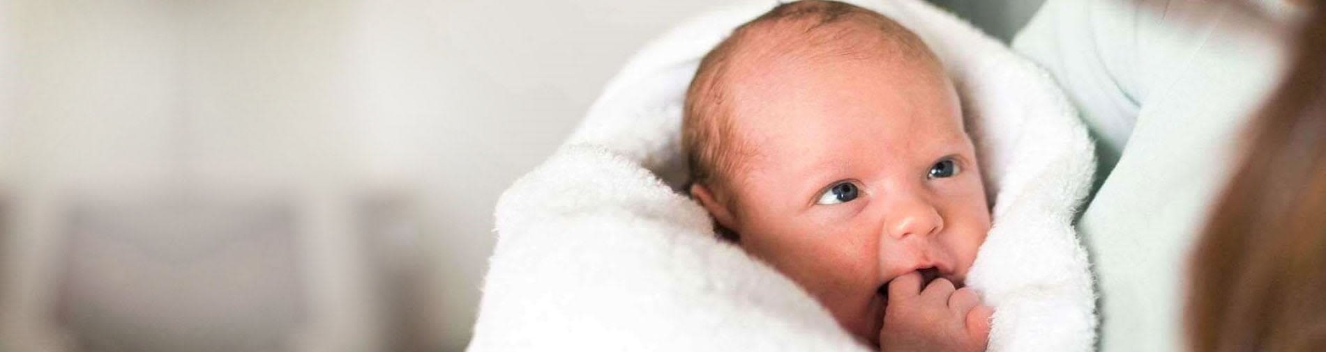 Newborn baby wrapped in a white blanket, looking towards the camera.
