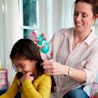 Mother using Johnson's baby No More Tangles Detangling Spray and combing daughter's wet hair, both smiling in a bright room.
