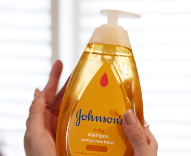 Mulher sorrindo, aplicando shampoo Johnson's Baby nos cabelos