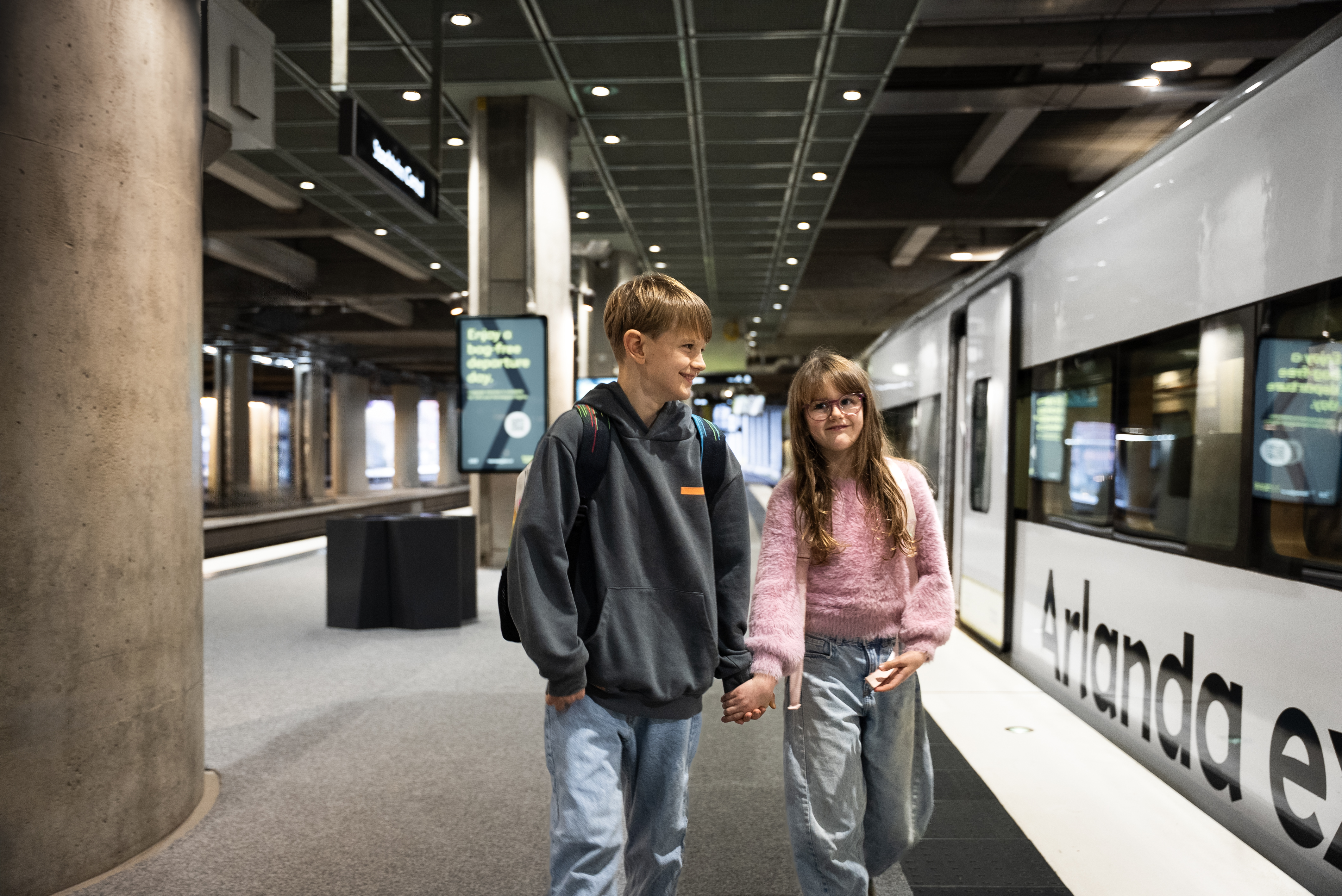 Two children walk along the Arlanda express platform holding hands at Stockholm Central Station.