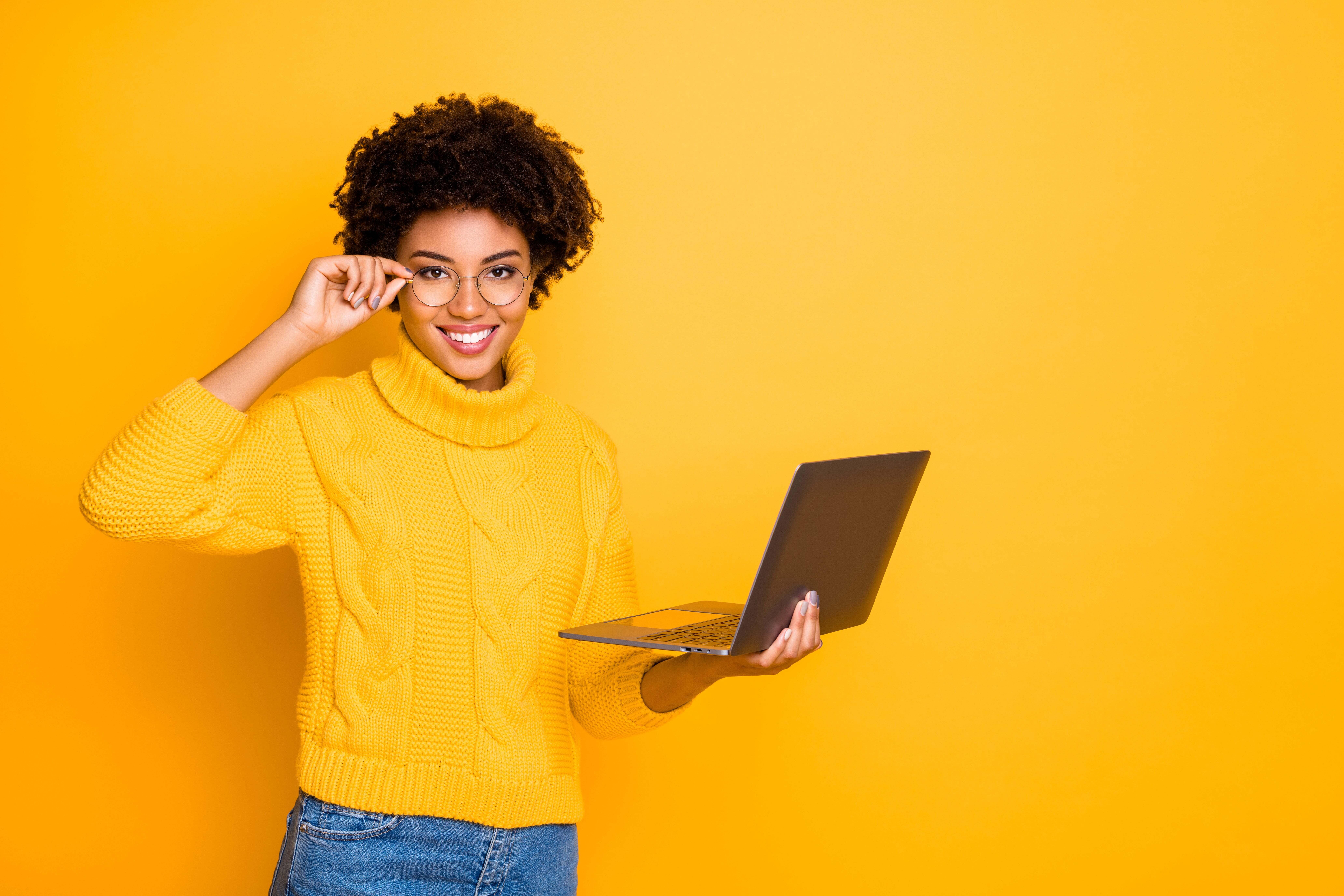 A woman wearing glasses with a laptop in her hand