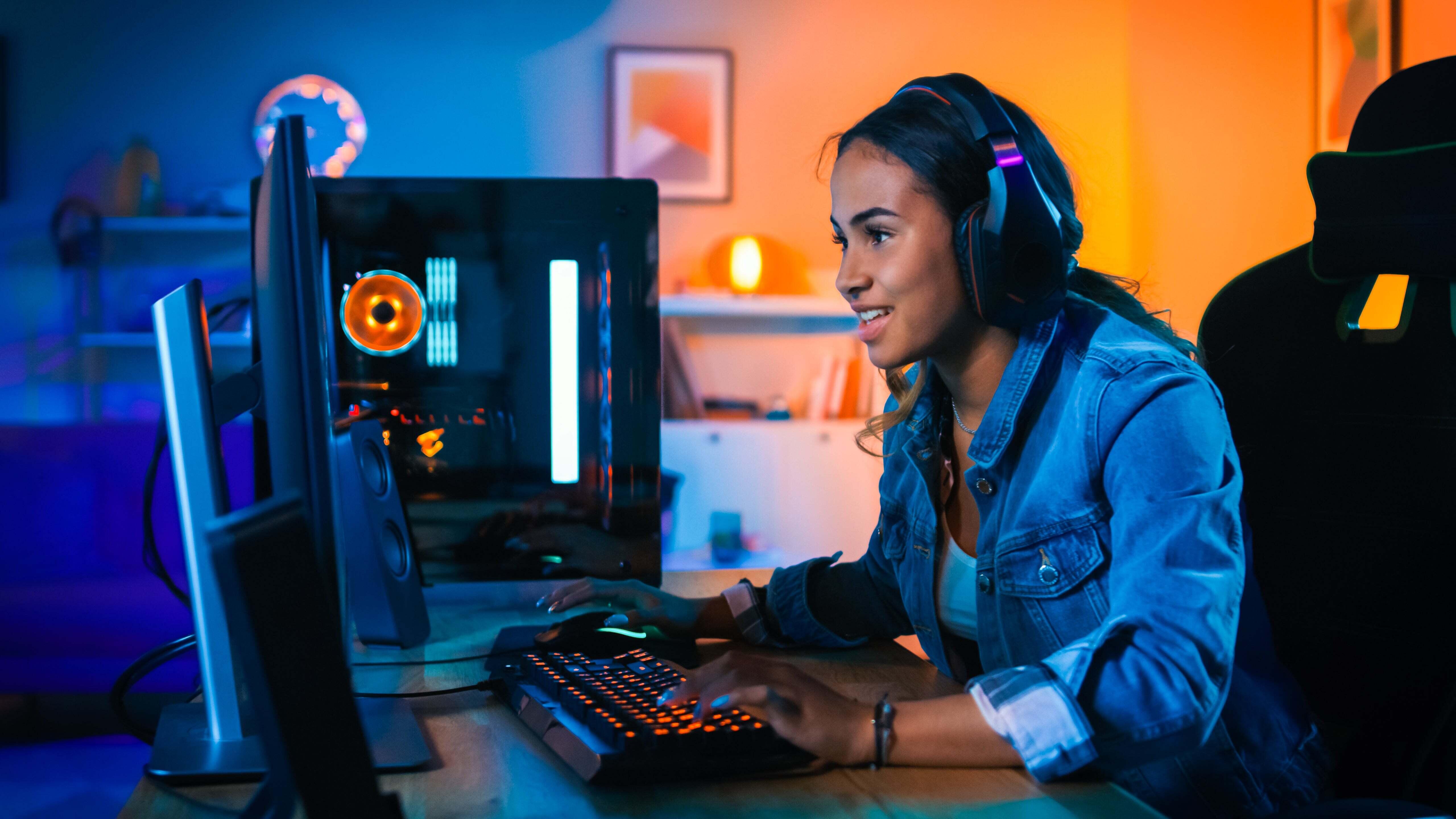 A woman with headphones playing on a computer at a gaming desk