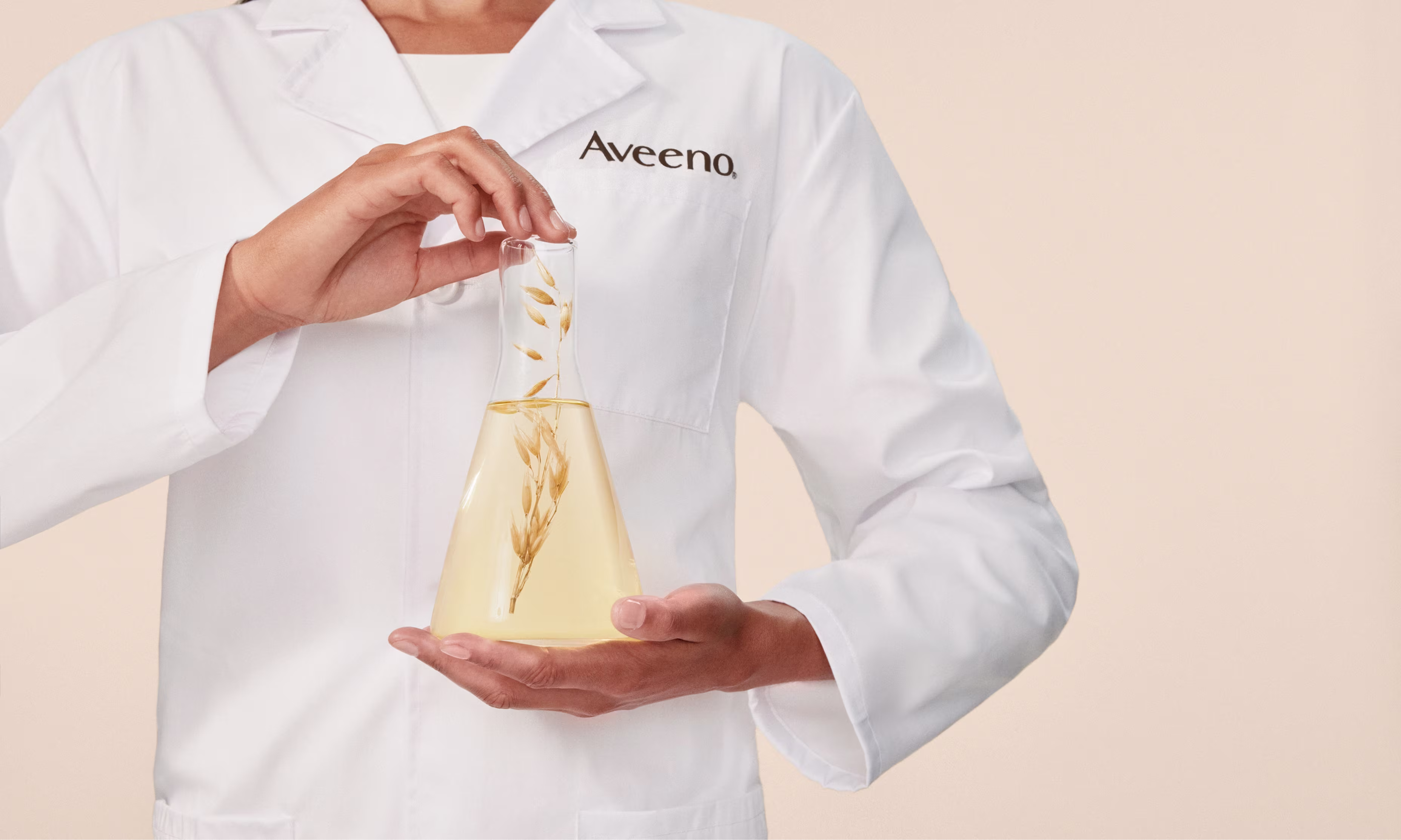 Person in a lab coat holds a glass with Oat leaves, showcasing her expertise in skincare research