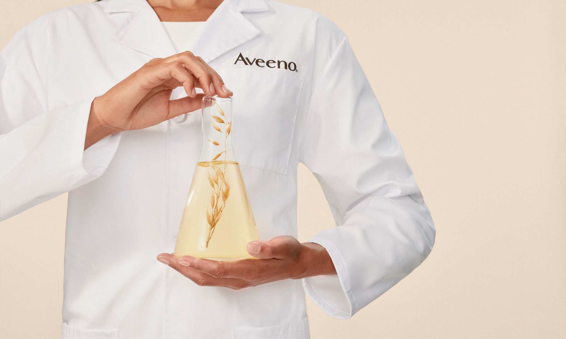 Person in a lab coat holds a glass with Oat leaves, showcasing her expertise in skincare research