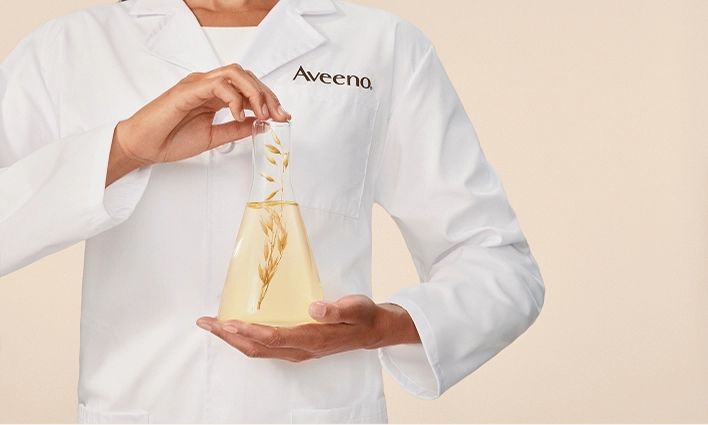 Aveeno scientist showcasing oat extract in a lab flask for skincare innovation.