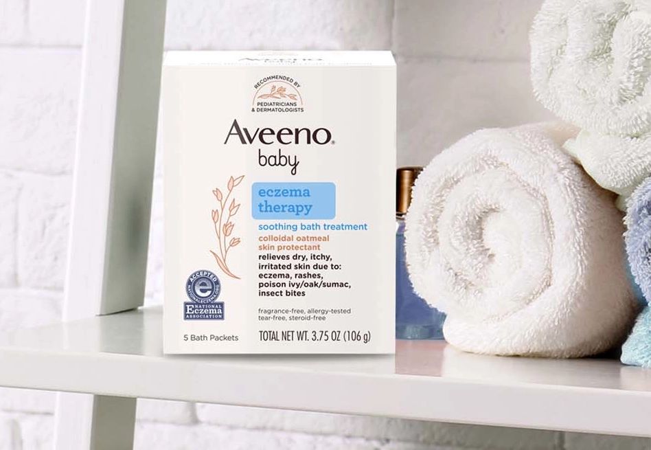 Aveeno® Baby Eczema Therapy soothing bath treatment package with some towels beside