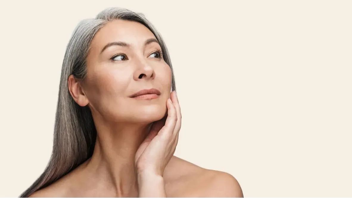 Older woman with gray hair gently touching her cheek looking to the side
