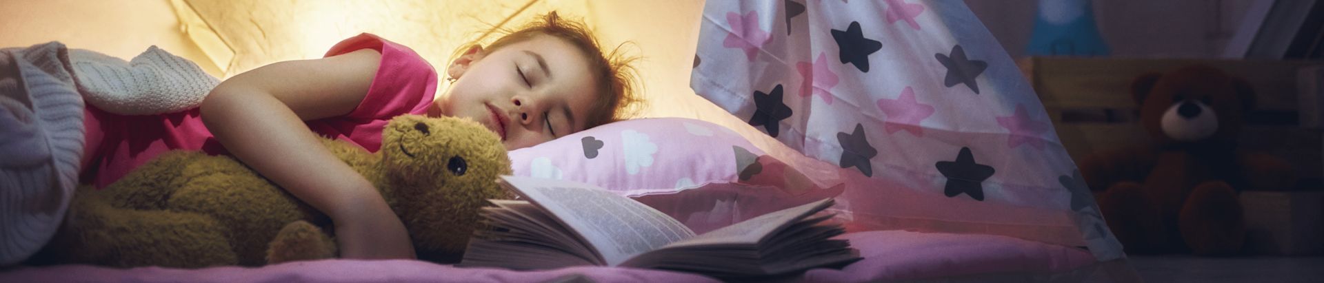 A little girl peacefully sleeps with a teddy bear nestled in her arms, surrounded by soft blankets