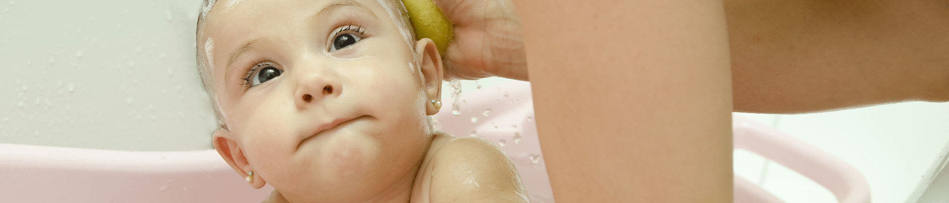 A baby getting a bath while being gently washed with a sponge in a pink bathtub.