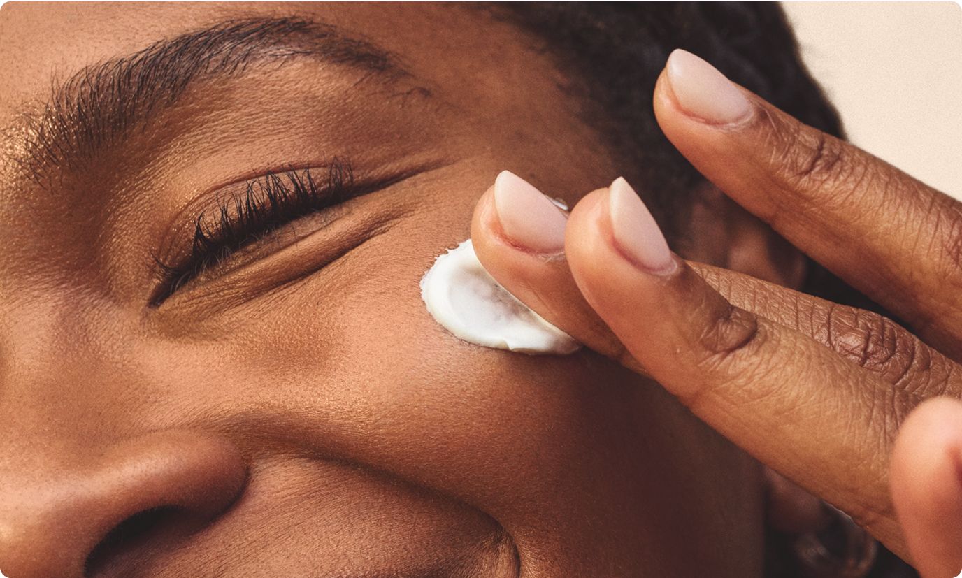 A woman smiling and softly massage her face with a light texture lotion