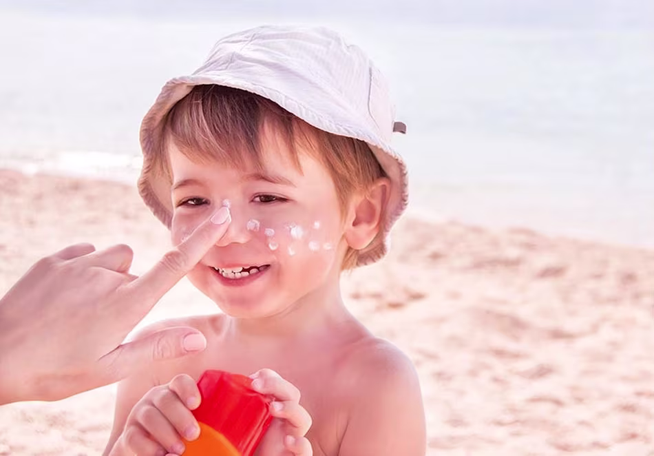 A child at the beach with sunscreen applied to his face, smiling and enjoying the sunny day