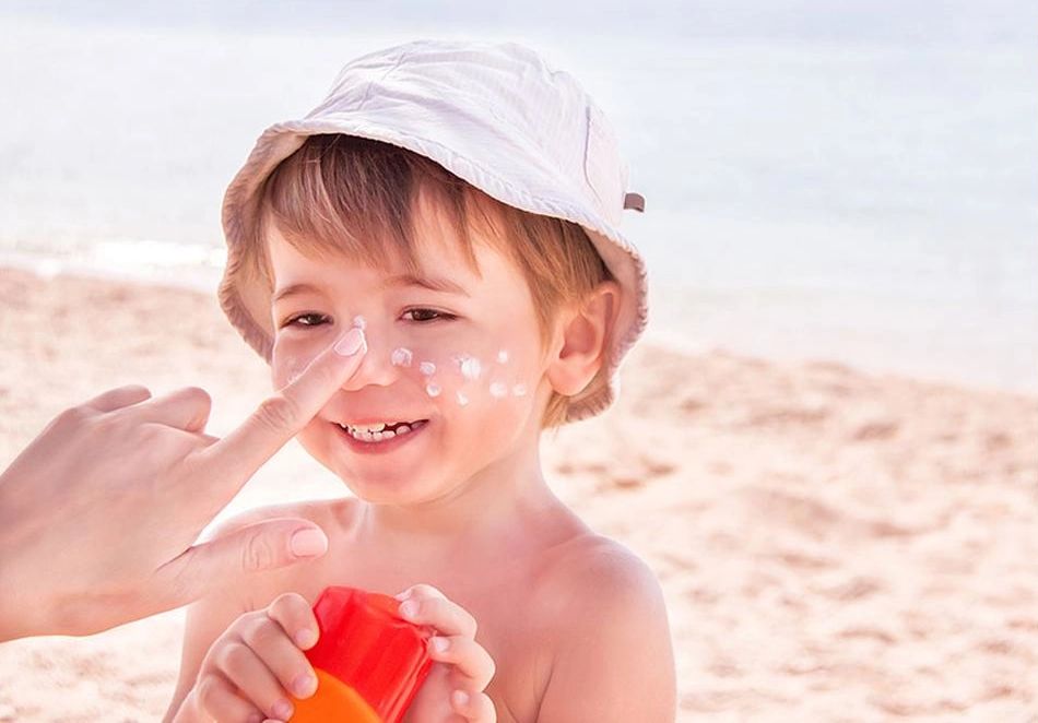 A child at the beach with sunscreen applied to his face, smiling and enjoying the sunny day