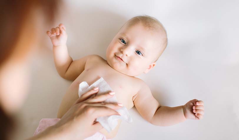 Infant lying on a light surface while a caregiver uses a wet wipe on their chest or abdomen