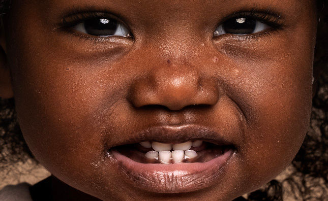 Close-up of a young child beaming with a joyful, toothless smile, radiating innocence and happiness