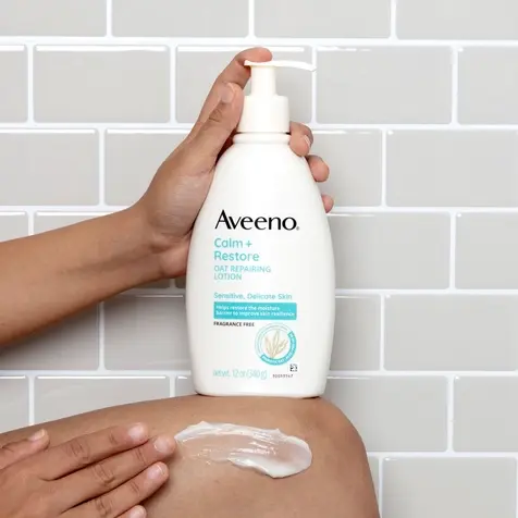 Close up of a person holding Calm + Restore Oat Repairing Lotion with one hand and applying it with the other on their leg
