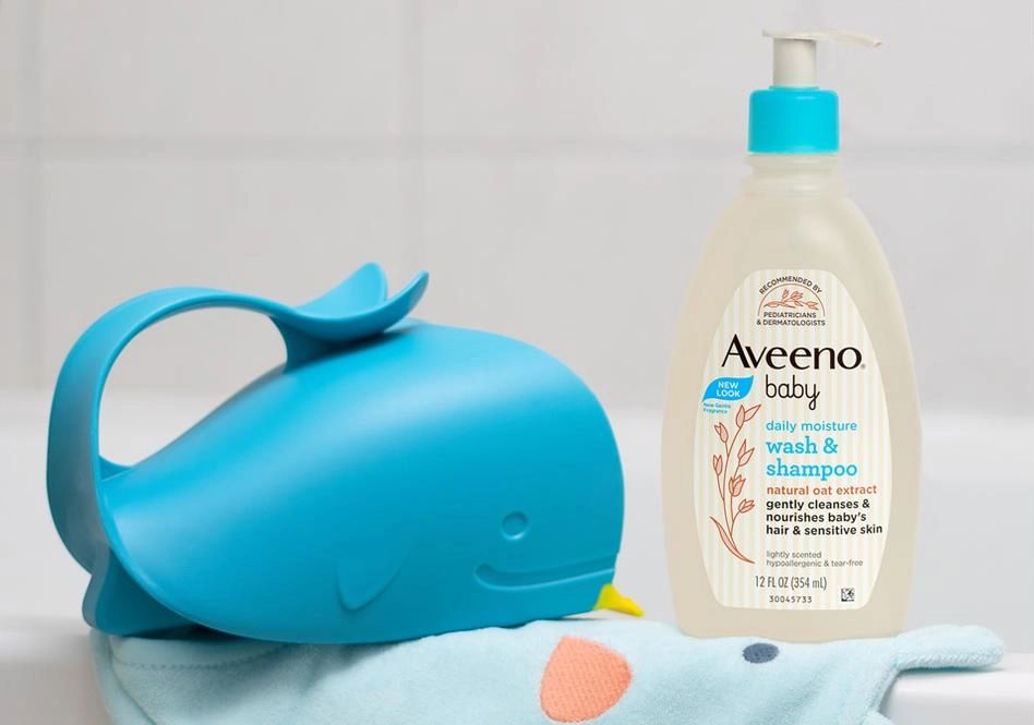 Aveeno® Baby Wash & Shampoo and a whale toy placed on a baby towel sitting on the edge of a bathtub