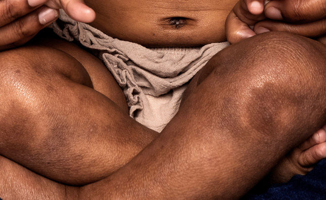 Close up of baby sitting with legs crossed, showing belly, knees and shins