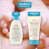 Front shot of Aveeno® Baby Healthy Start Newborn Wash and Balm products and close-up of baby's foot in parent's palm in the background