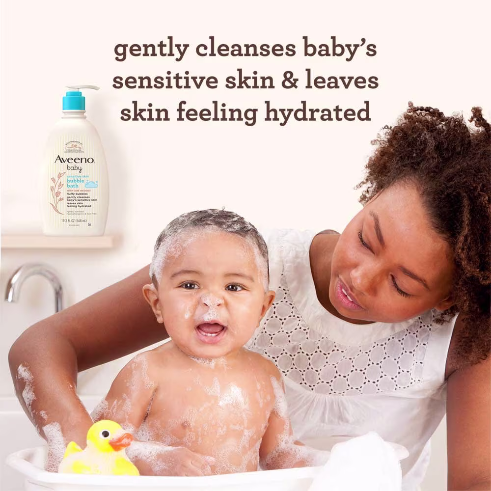 Woman bathing baby in a small bathtub with Aveeno® Baby Bubble Bath bottle in the background.