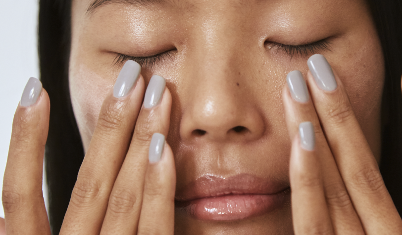 A woman with her hands on her face, she's applying product under her eyes