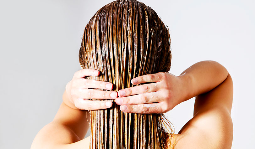 Person with wet, light brown hair applying a treatment product, such as a deep conditioner
