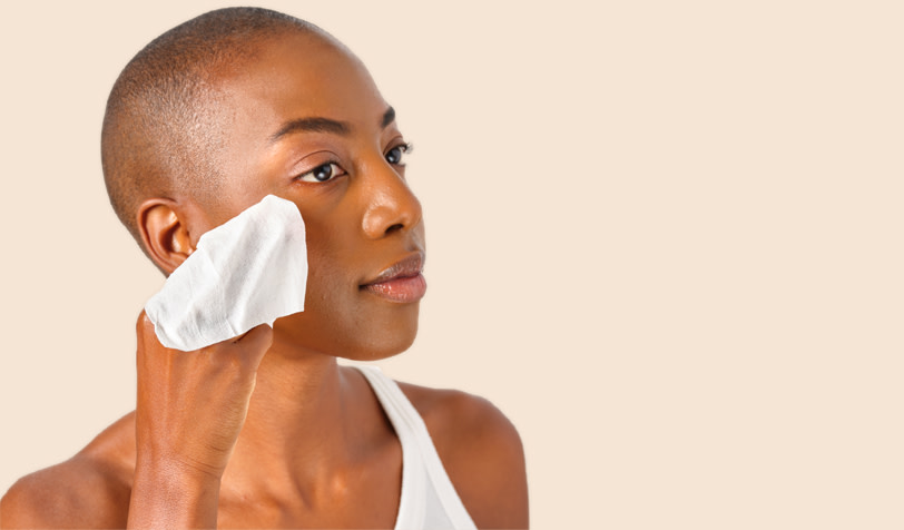A woman with a slight smile uses a make-up remover wipe on her face, showing self-care
