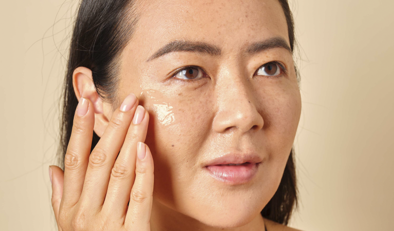 An asian woman rubbing cream to her face, showcasing her skincare routine and radiant complexion