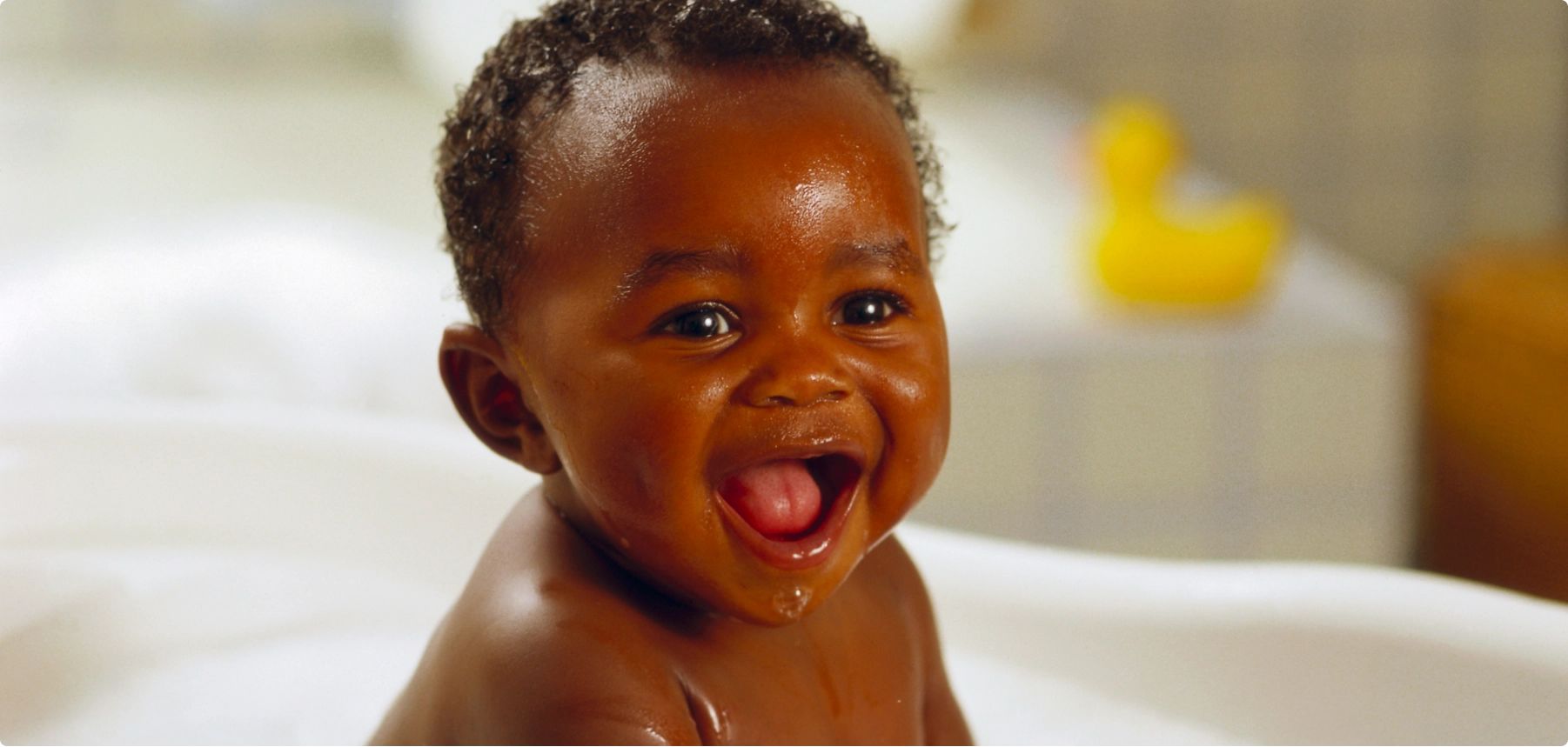 A joyful baby smiles while sitting in a bathtub filled with bubbles