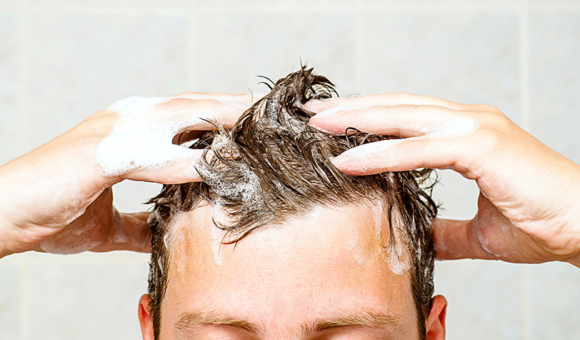 Person with brown hair massaging white soapy lather into their scalp during a hair wash