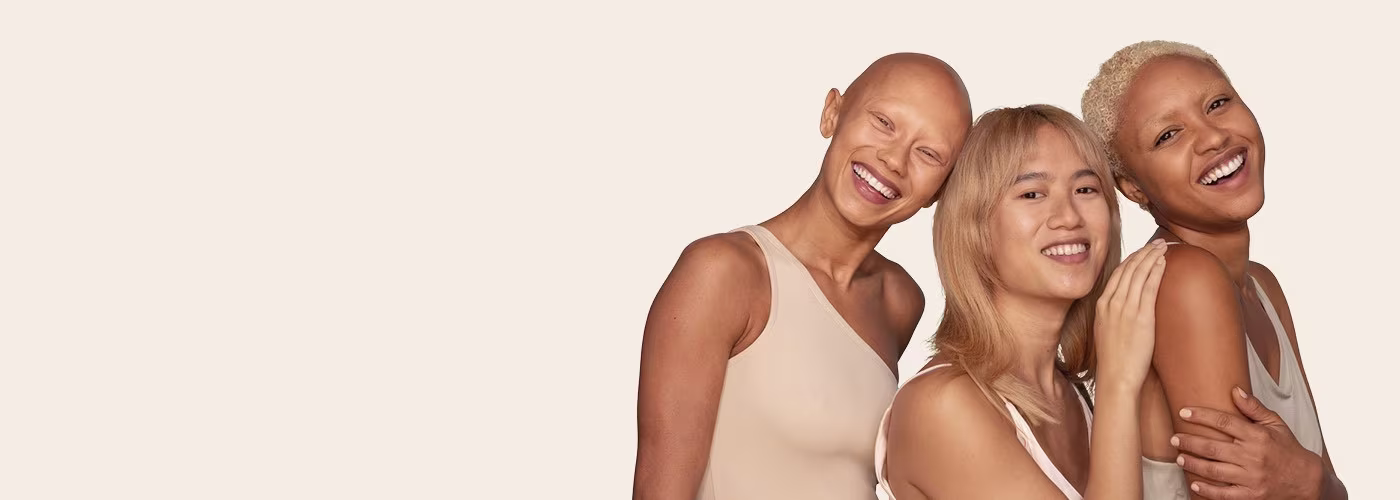 Trois femmes d'ethnies différentes se tiennent ensemble en sourient.