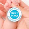 Aveeno® Baby product claim indicating 'Safe For Day One' and close-up of parent's hand holding their newborn baby's hand in the background