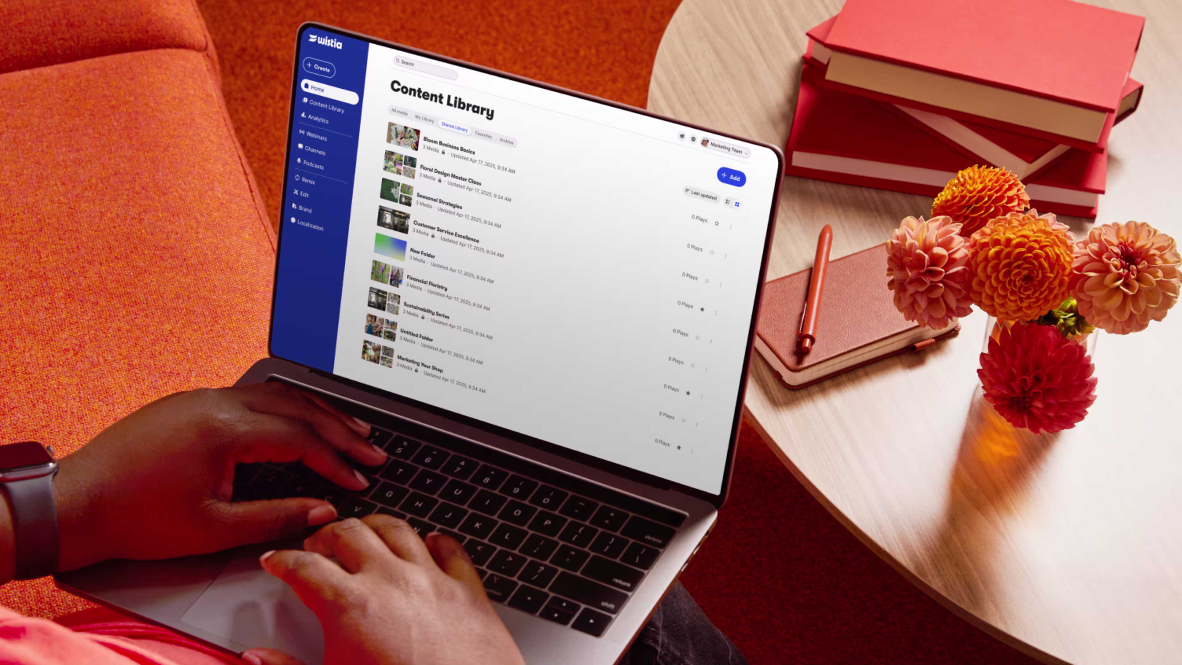The hands of someone typing away on a laptop. Screen shows the Wistia content library.