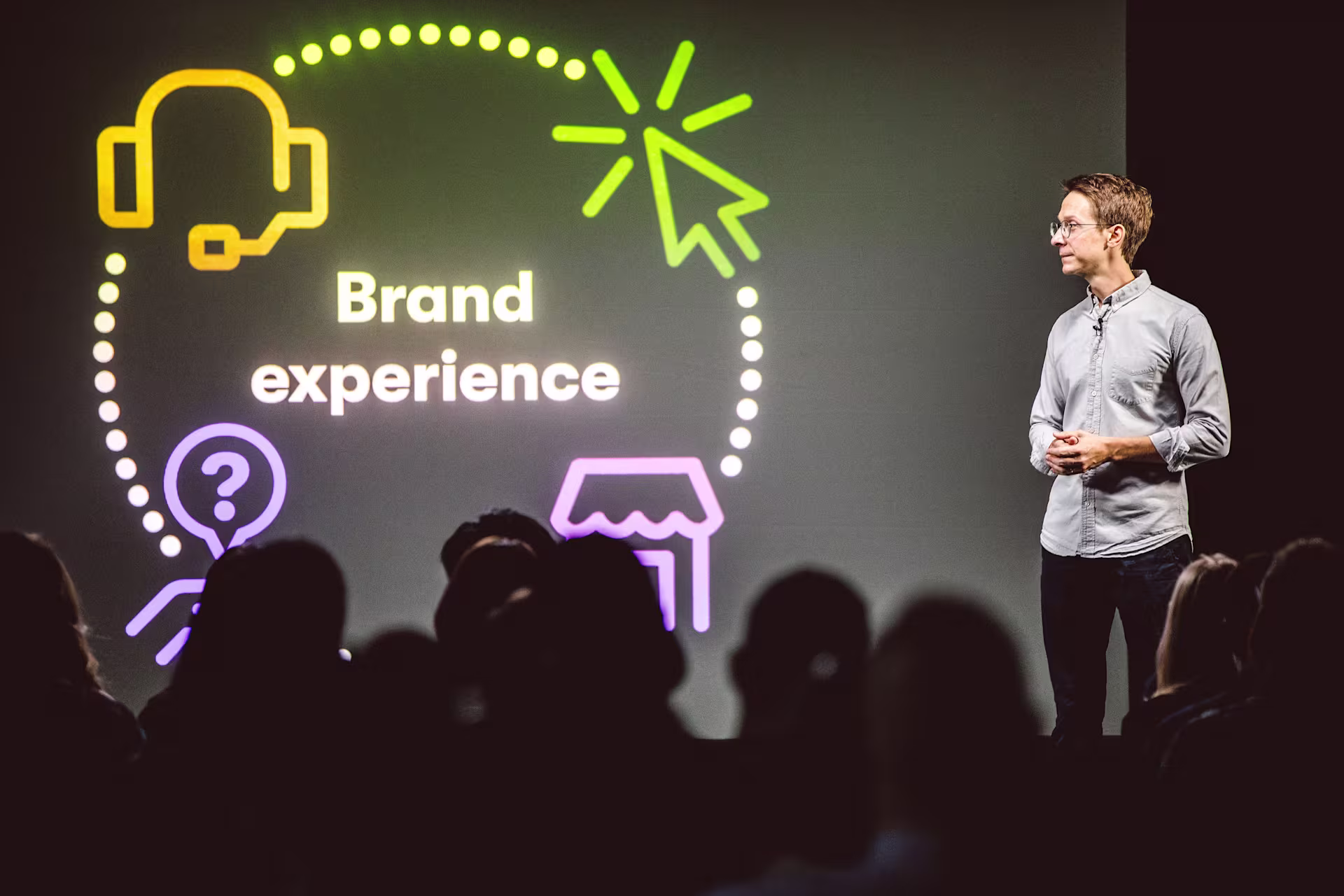 a man standing on stage in front of a screen that says, "Brand experience"