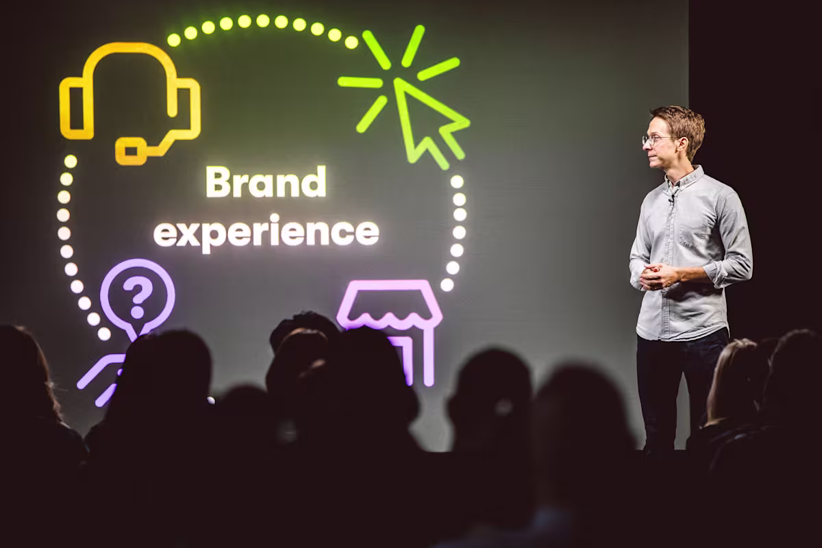a man standing on stage in front of a screen that says, "Brand experience"