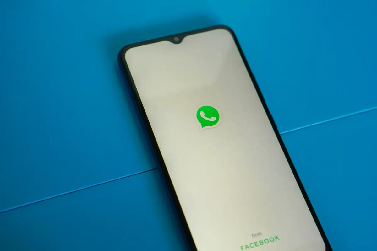 A smartphone displaying the WhatsApp logo on its screen against a blue background
