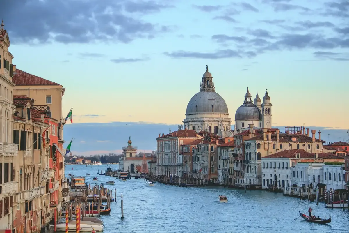 A canal lined with historic buildings and domed churches, with boats and gondolas on the water