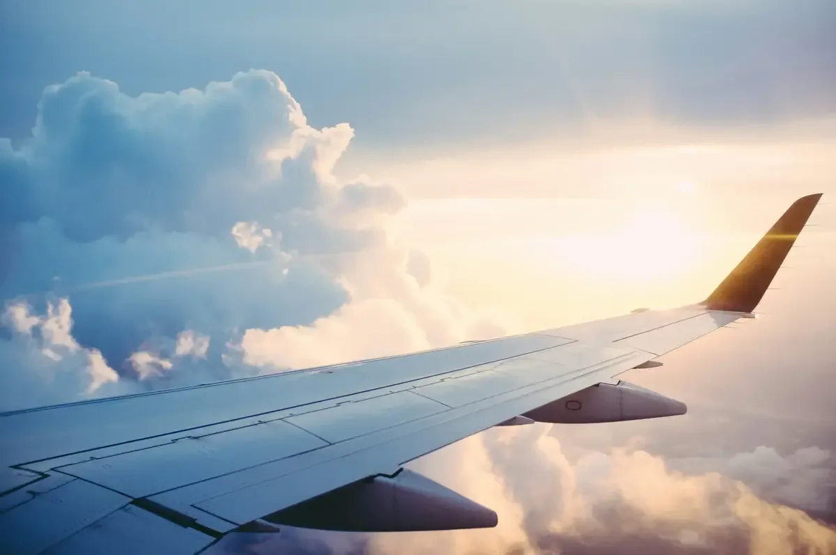 Airplane wing flying above clouds at sunrise