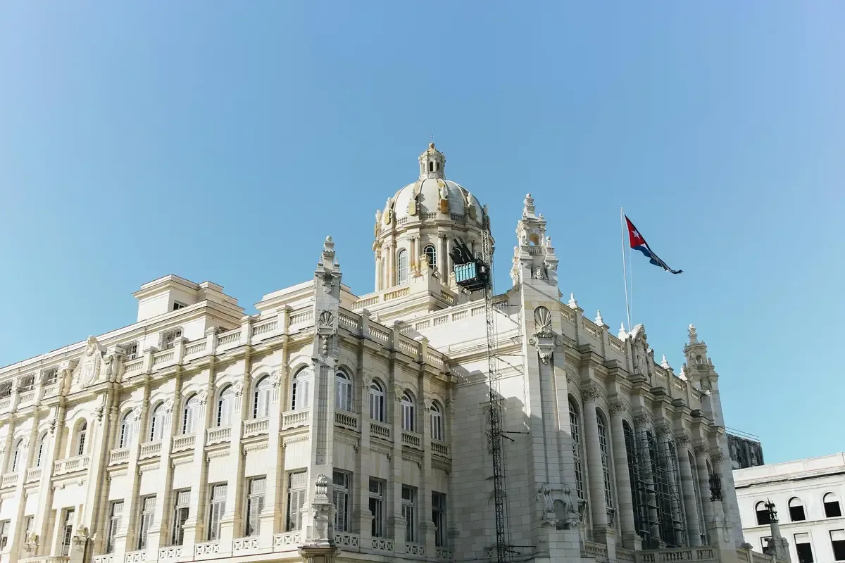 Neoclassical building with dome and Cuban flag under a clear blue sky