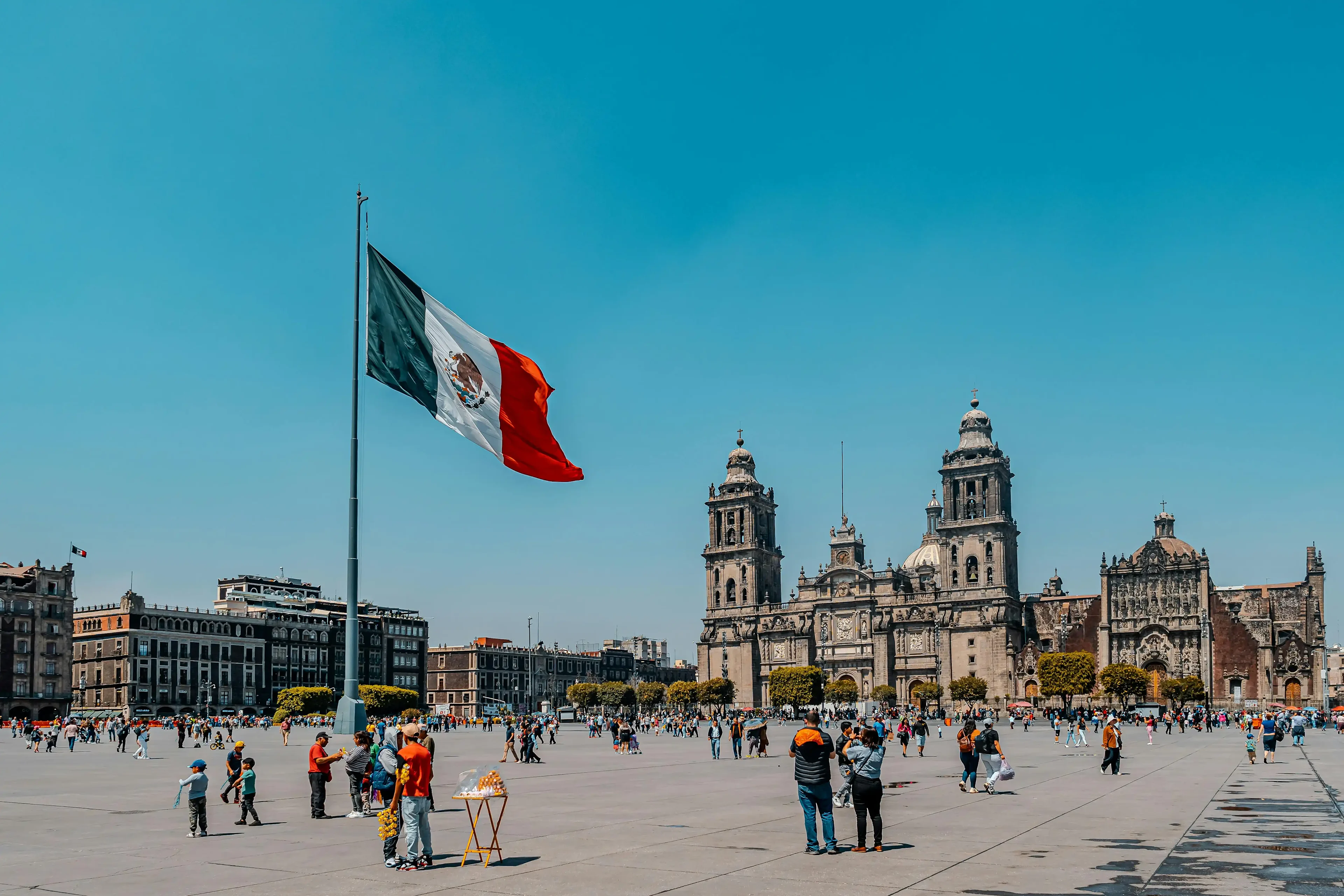Mexico City's Zócalo with people, Mexican flag, and cathedral under clear sky